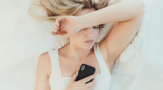 woman-in-bed-on-her-cellphone-with-one-arm-up